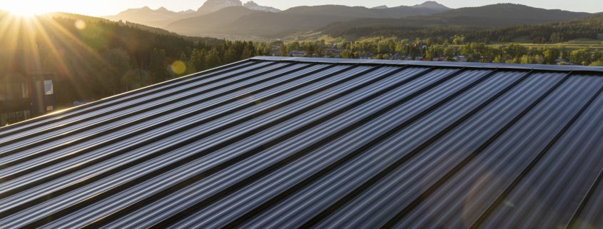 Dark standing seam metal roof against a scenic mountain sunset background.